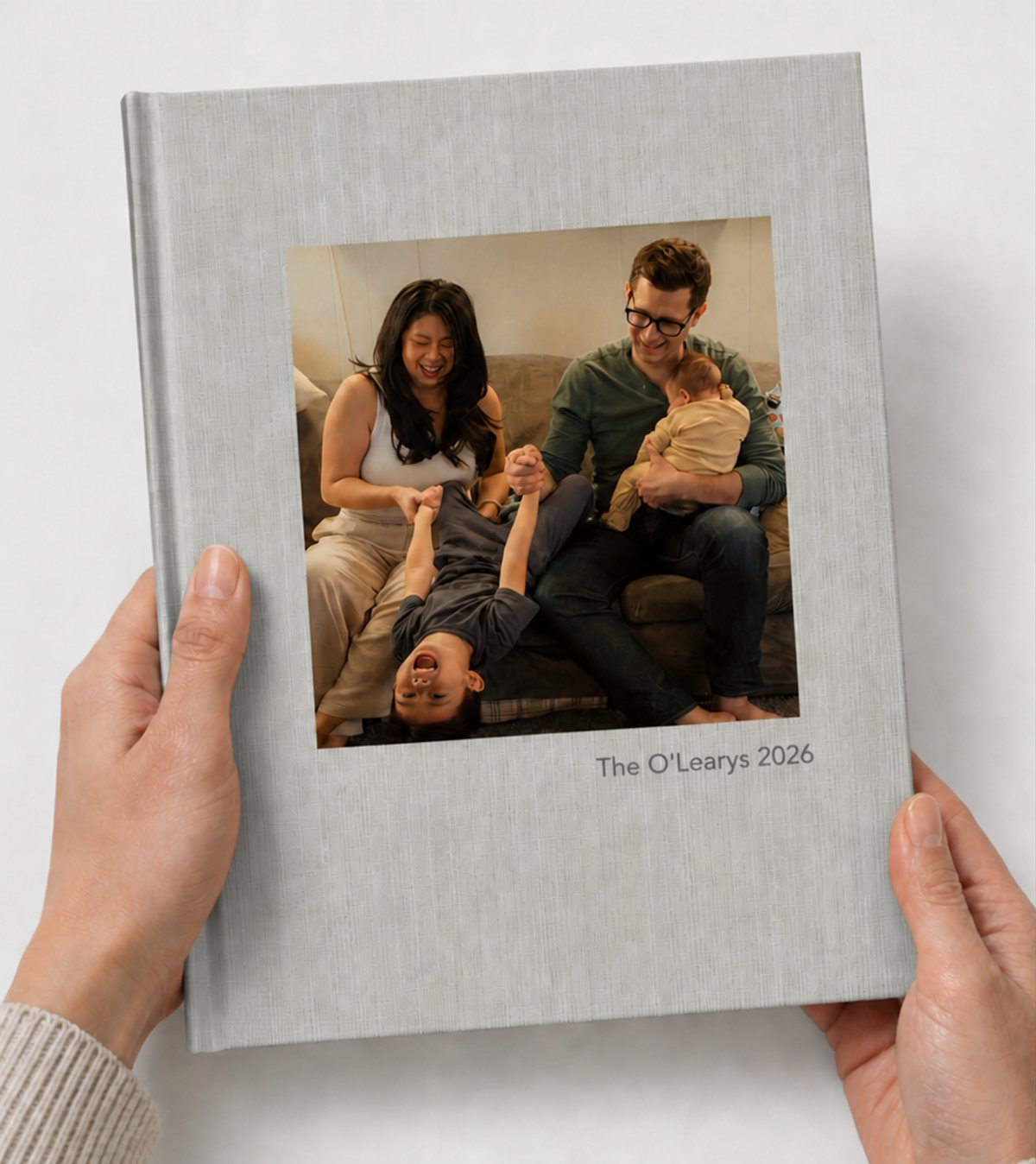 Hands holding a closed linen hardcover book titled &lsquo;The O&rsquo;Learys 2026&rsquo; with a family photo on the cover