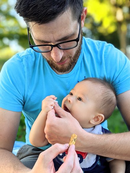 A parent feeding a baby a snack outdoors